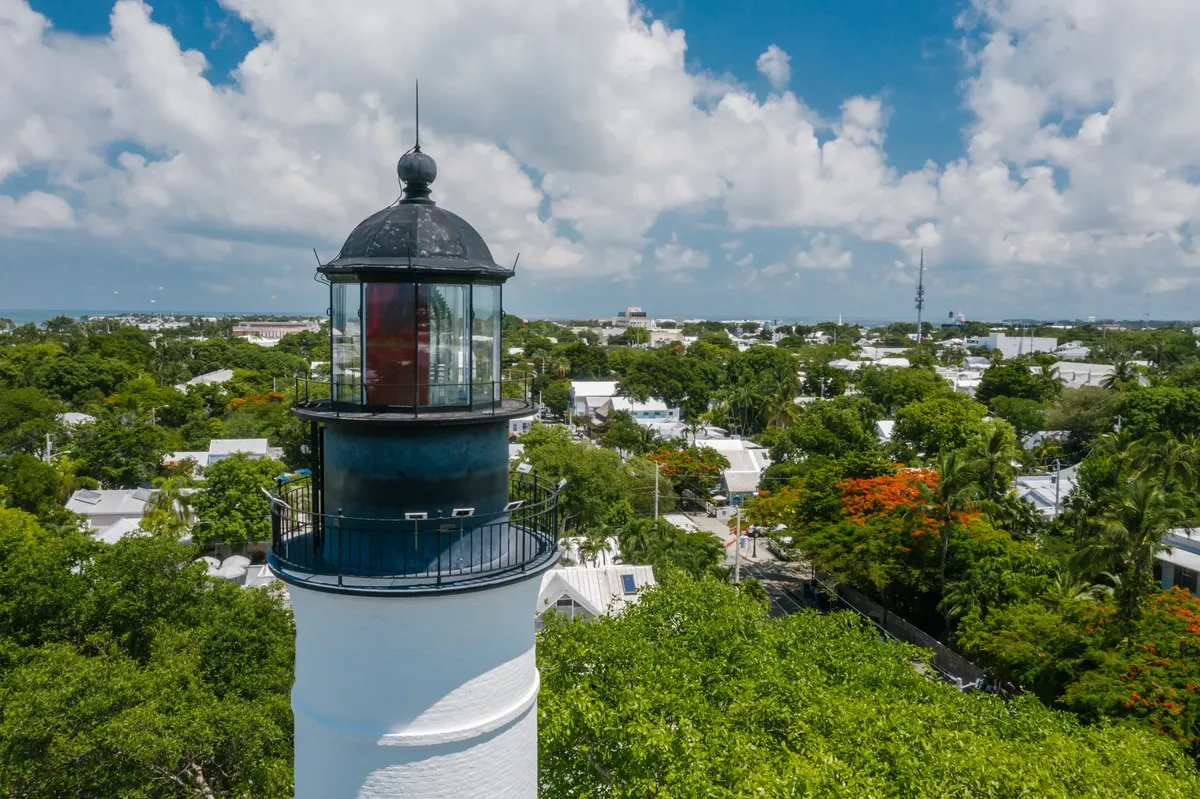 Discover the historic Key West lighthouse surrounded by lush greenery under a bright blue sky.